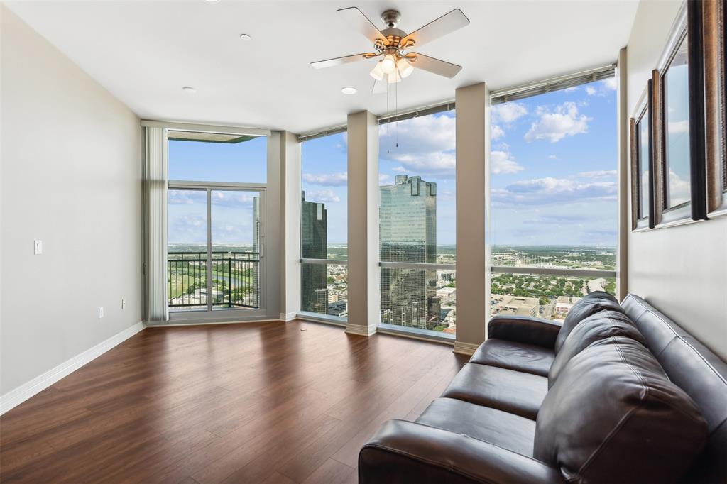Floor-to-ceiling windows, wood-finish flooring, sliding glass door with access to a balcony, and a ceiling fan with integrated light fixture