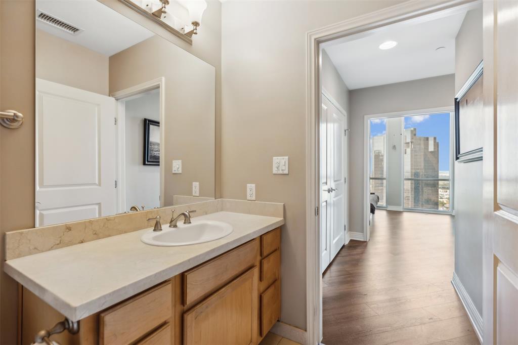 Bathroom featuring a wood-finish vanity with a stone countertop, integrated sink, and large wall-mounted mirror, paired with wood-finish flooring throughout the interior