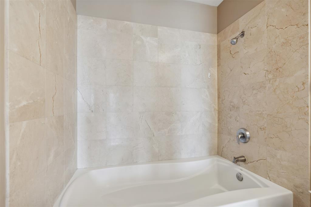 Bathtub with a white acrylic surround, wall-mounted polished chrome fixtures, and neutral stone-finish tile wall cladding