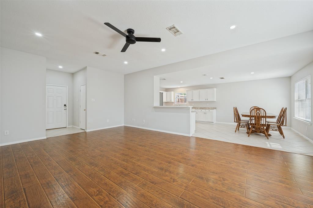 Open-concept interior featuring wood-finish flooring, a matte black ceiling fan, recessed lighting, and white cabinetry in the kitchen