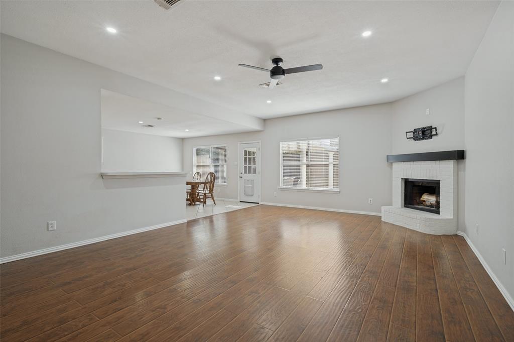 Wood-finish flooring, corner fireplace with a white brick surround, dark mantel, recessed lighting, and ceiling fan