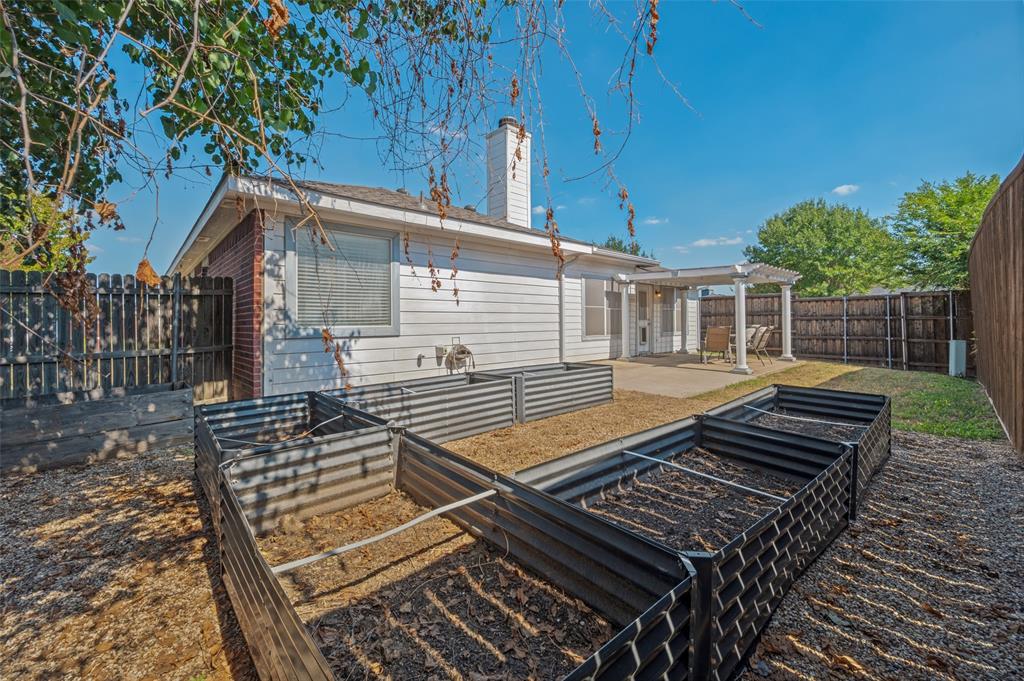 Backyard featuring elevated metal garden beds, a concrete patio, a covered pergola with columns, a masonry chimney, and perimeter wood fencing