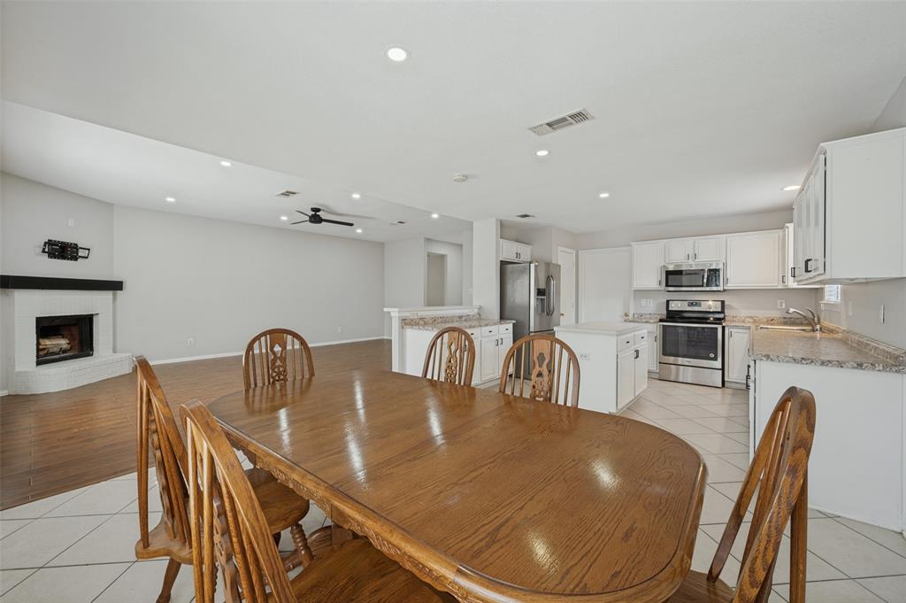 Open-concept living space featuring wood-finish flooring, a masonry fireplace with a mantel, recessed lighting, white cabinetry, and a central kitchen island