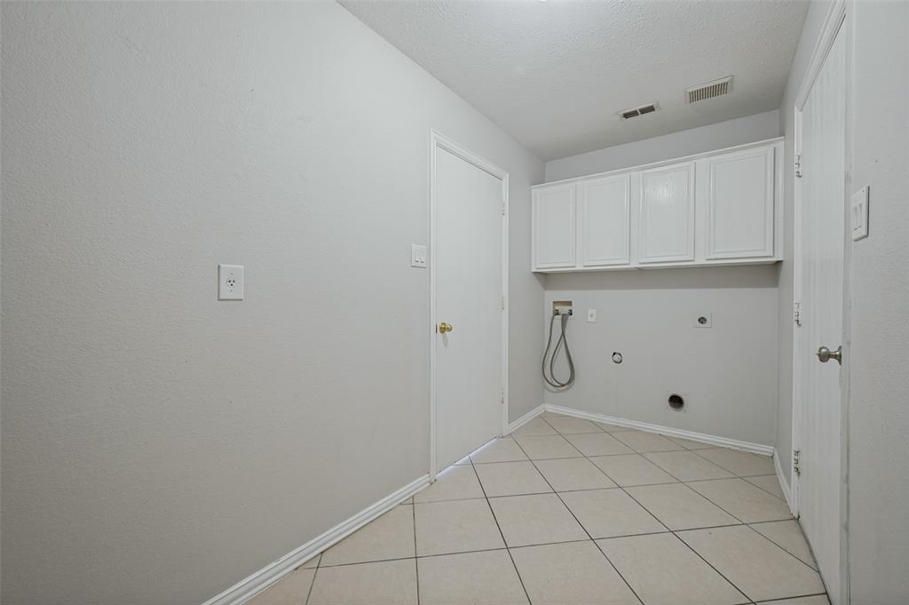Utility area featuring light-toned tile flooring, white shaker-style wall-mounted cabinetry, and dedicated washer and dryer hookups