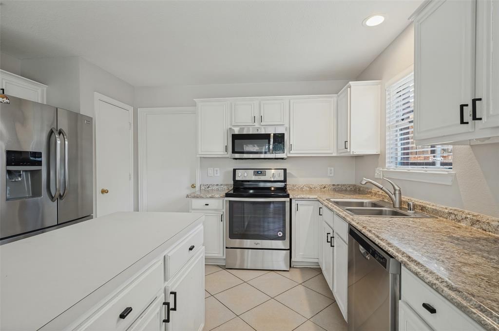 Kitchen featuring white cabinetry, stone-finish countertops, stainless steel appliances, a kitchen island, and ceramic tile flooring