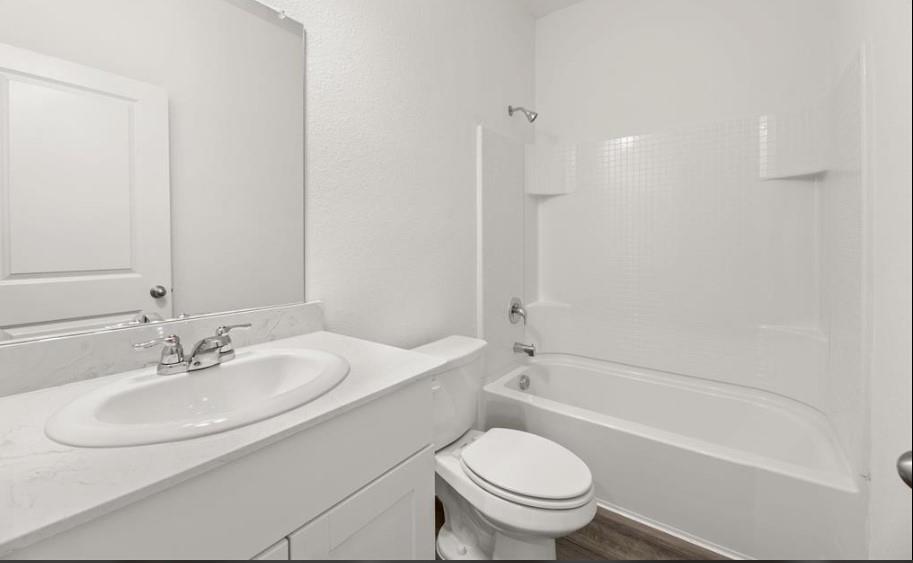 Bathroom featuring a vanity with a white countertop and oval under-mount sink, white paneled cabinetry, large wall-mounted mirror, and a tub-shower combination with a white surround