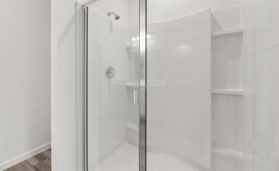 Walk-in shower featuring a curved glass enclosure, smooth white surround panels, integrated shelving, and a chrome shower fixture