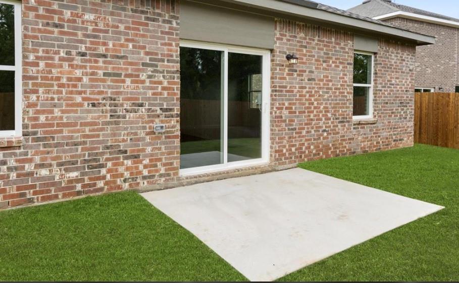 Exterior featuring red brick masonry, a concrete patio, sliding glass door, white-framed windows, and a wood privacy fence
