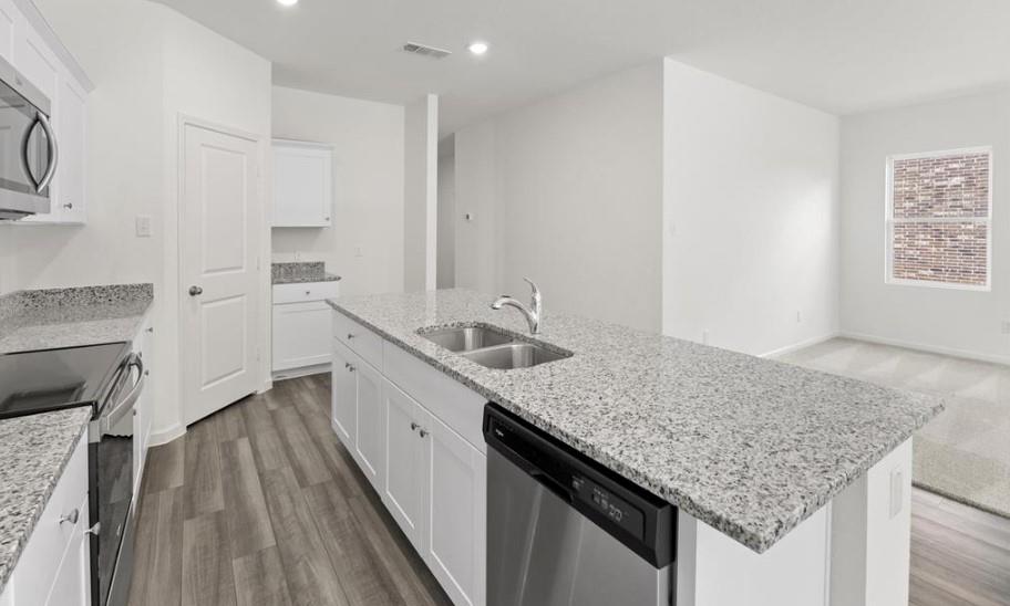 Kitchen featuring a central island with a double-basin stainless steel sink, speckled stone countertops, shaker-style white cabinetry, stainless steel appliances, and wood-finish flooring