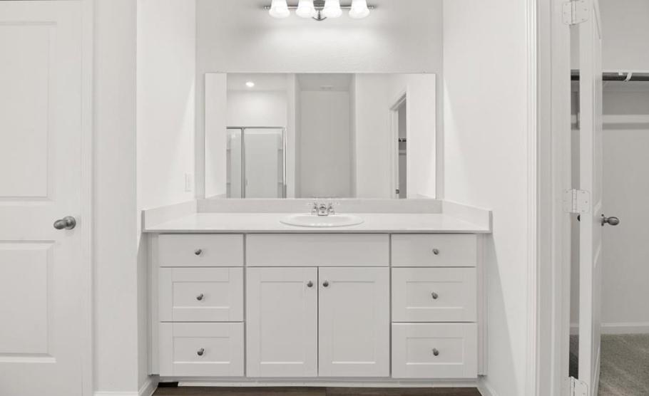 White vanity featuring shaker-style cabinetry, an integrated oval sink, solid-surface countertop, and a full-width wall mirror with a multi-bulb light fixture