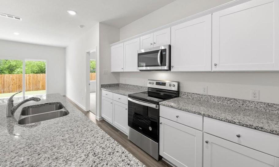 Kitchen featuring white shaker-style cabinetry, stone-finish countertops, stainless steel appliances, and a double-basin undermount sink