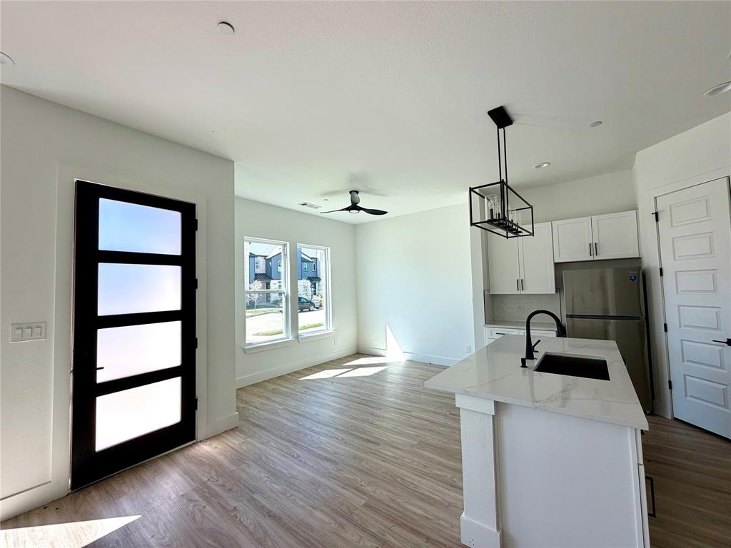 Open-concept interior featuring wood-finish flooring, a kitchen island with stone-finish countertops, matte black plumbing fixtures, white shaker-style cabinetry, and a multi-panel glass entry door