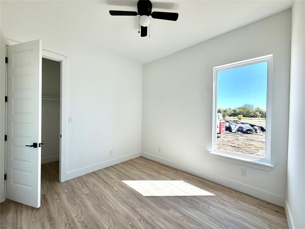 Interior space featuring wood-finish flooring, a five-panel interior door, a ceiling fan with integrated lighting, and a window with a exterior landscape outlook