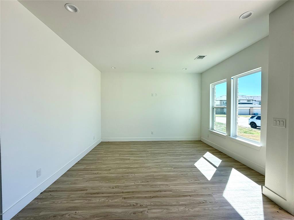 Open-concept room featuring neutral wall tones, wood-finish flooring, dual windows with exterior exposure, and recessed lighting