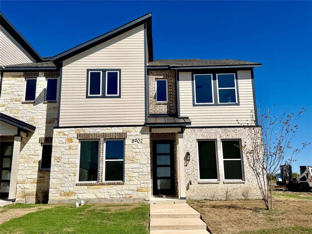 Multi-story exterior featuring a mix of stone veneer and horizontal siding, a pitched roofline, an entryway with a multi-pane glass door, and large rectangular windows with dark trim
