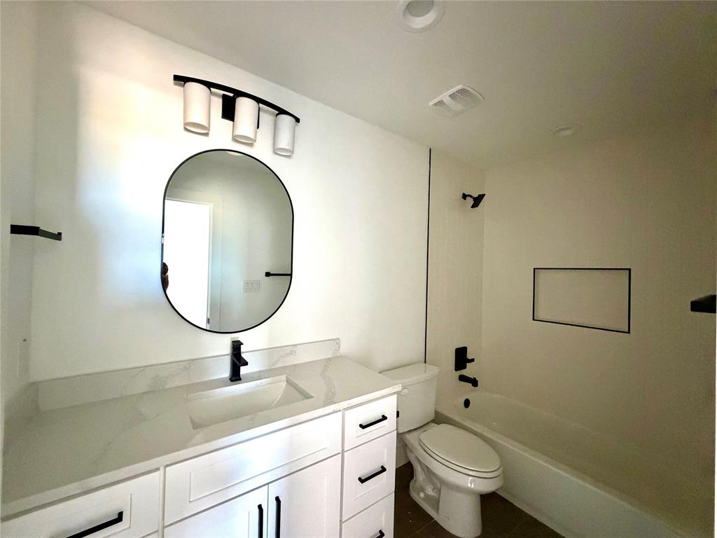 Bathroom featuring a vanity with stone-finish countertop, undermount sink, matte black fixtures, oval wall mirror, and a built-in shower niche