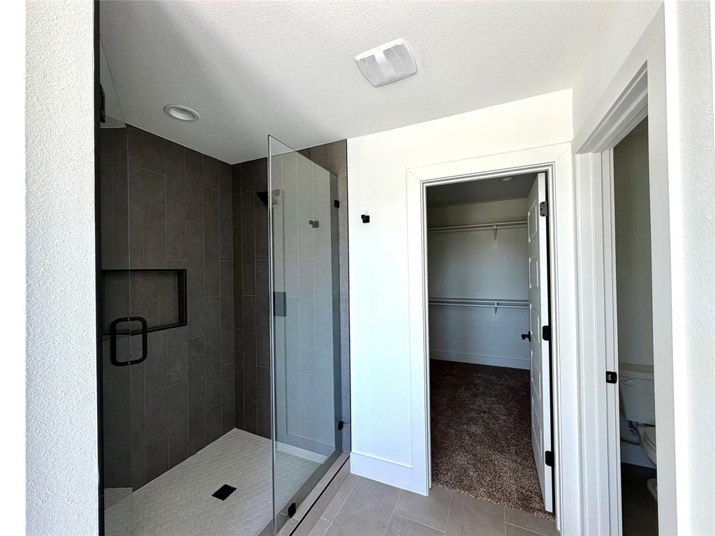 Walk-in shower with dark ceramic tile surround, built-in shelving niche, glass enclosure, and matte black hardware, accompanied by a separate carpeted closet space