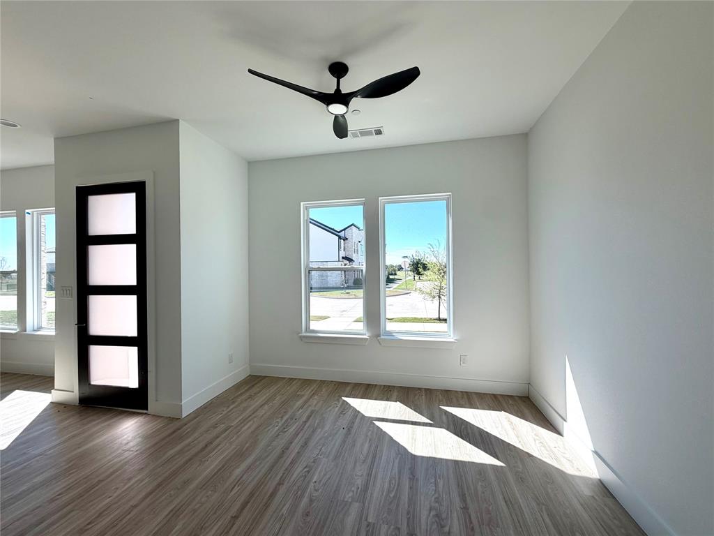 Wood-finish flooring, matte black three-blade ceiling fan with integrated lighting, and a modern single-panel door featuring four frosted glass inserts