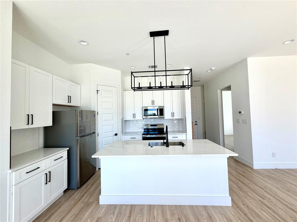 Kitchen featuring white cabinetry, center island with stone-finish countertop, stainless steel appliances, matte black hardware, and rectangular cage pendant lighting over wood-finish flooring