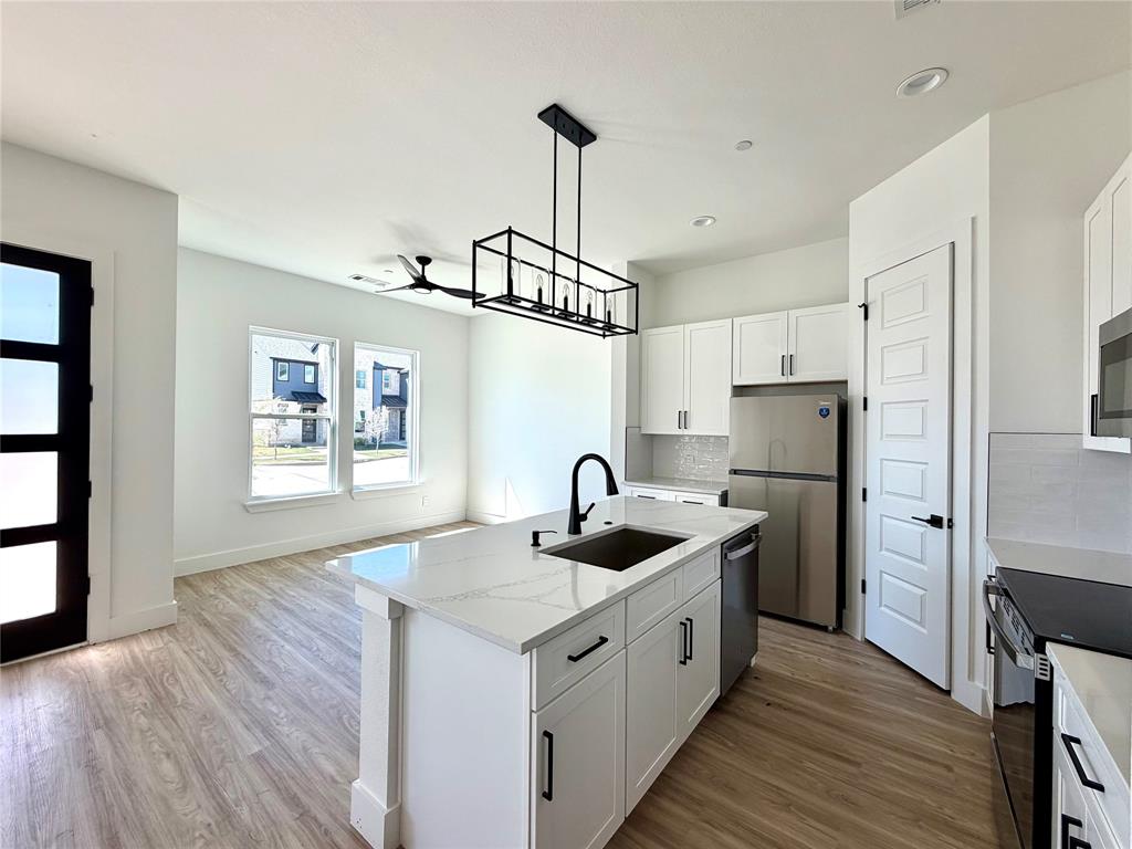 Kitchen featuring a central island with a stone countertop, white cabinetry, a matte black faucet, wood-finish flooring, and a linear pendant light fixture