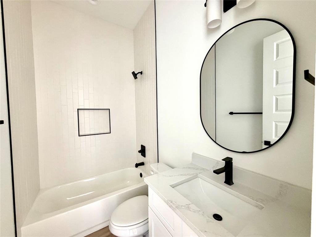 Bathroom featuring a vanity with a white countertop and rectangular undermount sink, matte black faucet, wall-mounted oval mirror, built-in tub with vertical white wall tile, and recessed shower niche