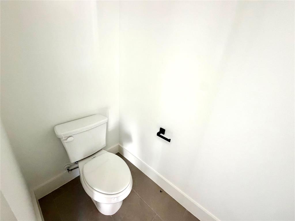 White vitreous china toilet, matte black toilet paper holder, and neutral large-format tile flooring