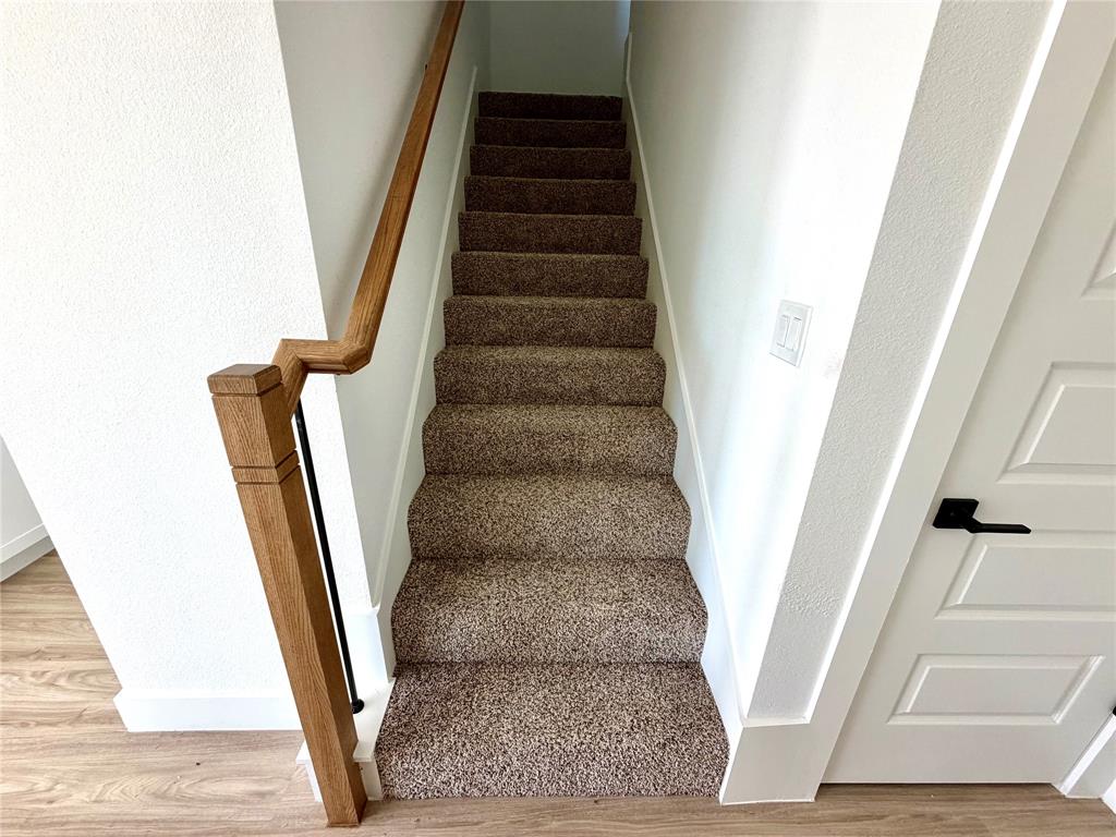 Staircase featuring wall-to-wall carpeting, wood-finish handrail, and matte black hardware on a four-panel interior door