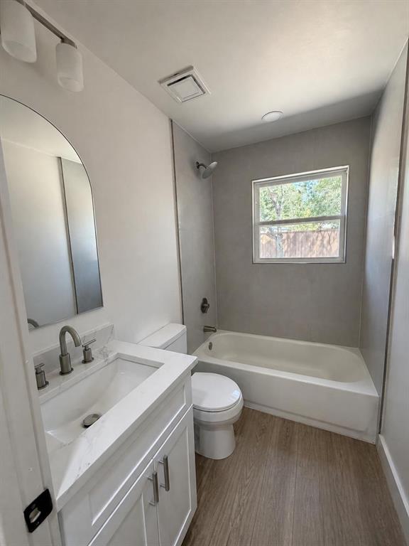 Bathroom featuring a vanity with a white countertop and rectangular undermount sink, arched wall mirror, brushed nickel faucet hardware, and wood-finish flooring