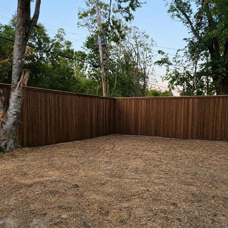 Outdoor area enclosed by a stained wood privacy fence, featuring mature trees and level terrain
