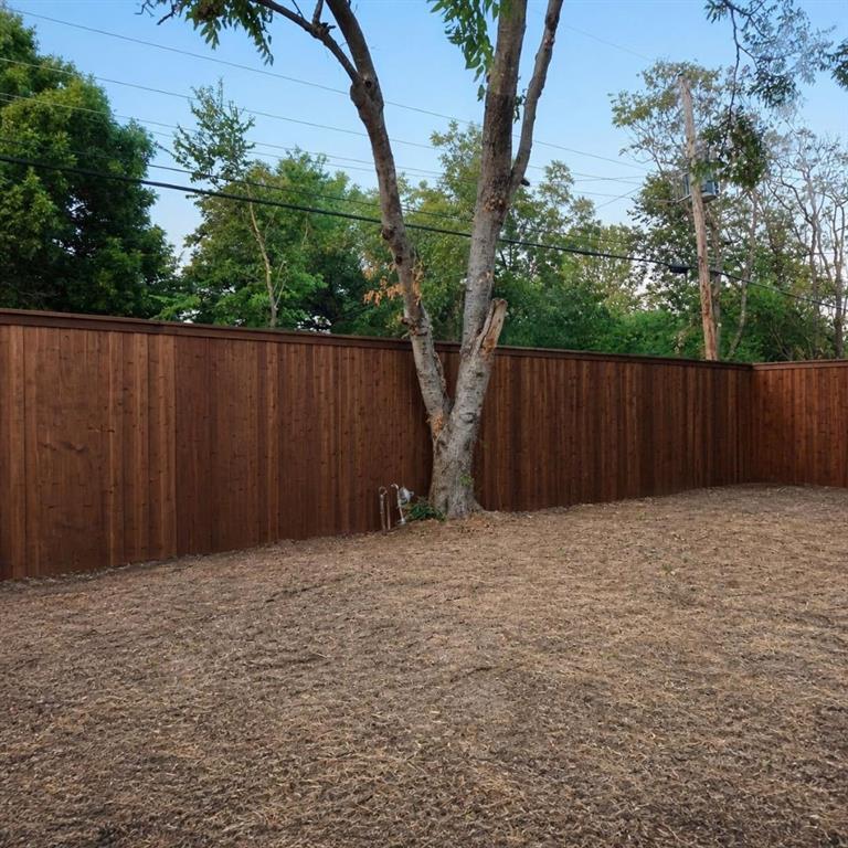 Rear yard featuring a tall, stained wood privacy fence and a mature tree