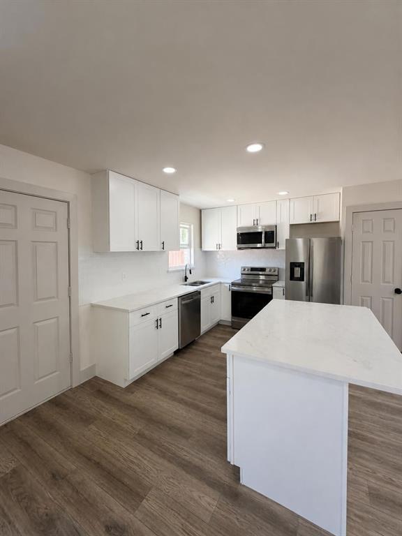 Kitchen featuring white cabinetry, stone-finish countertops, stainless steel appliances, a central island, and wood-finish flooring