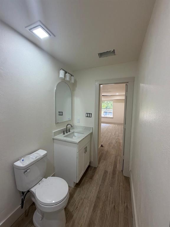White vanity with stone-surface countertop, under-mount sink, arched wall mirror, three-light fixture, and wood-finish flooring