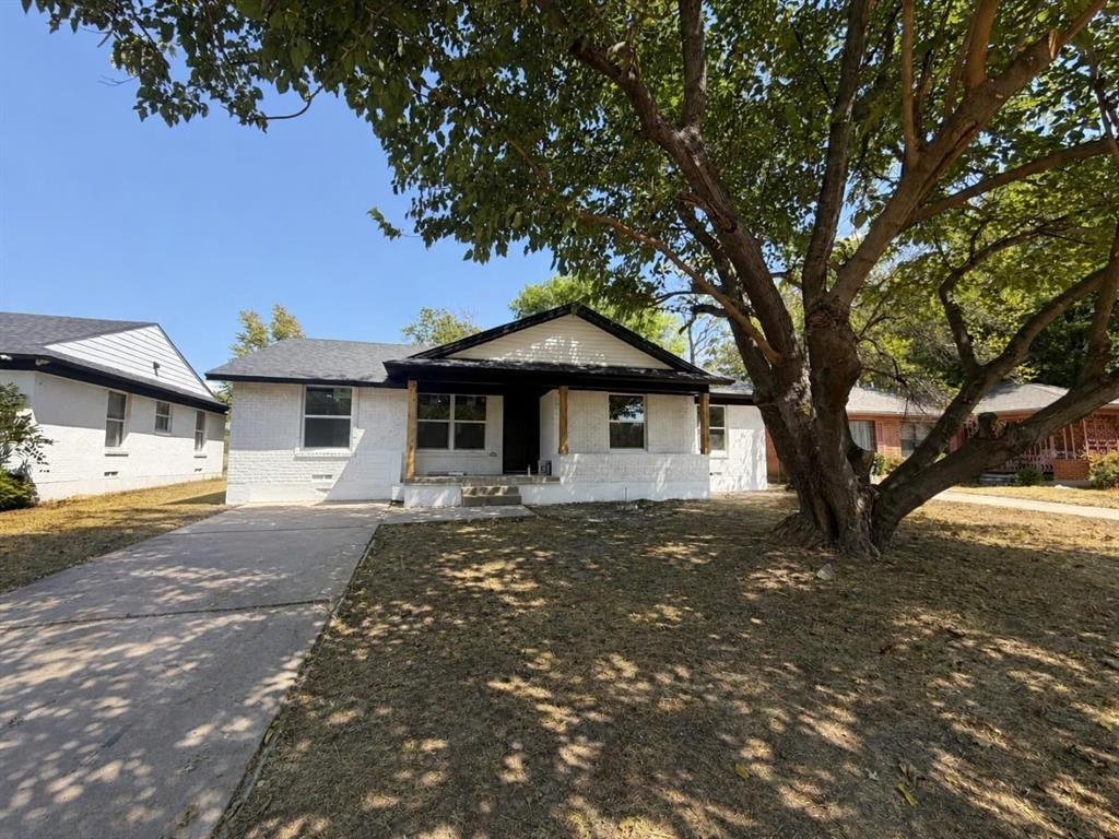 Single-story residence featuring a white painted brick exterior, gabled roofline, covered front porch with wood-finished support columns, and an attached concrete driveway