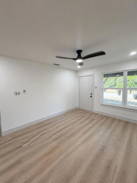 Interior space featuring wood-finish flooring, a matte black ceiling fan with integrated lighting, neutral wall finishes, and a six-panel exterior door