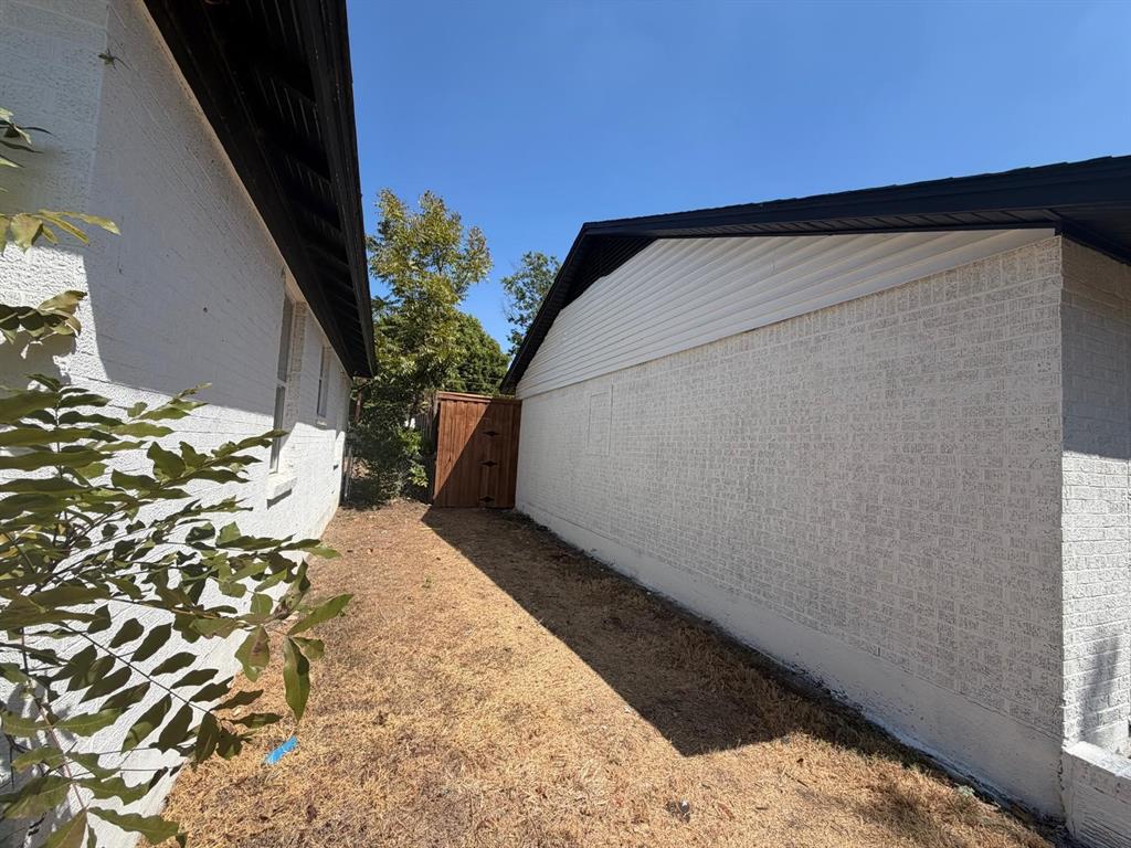 Exterior side yard featuring white painted brick masonry, horizontal siding gables, and a wood privacy gate