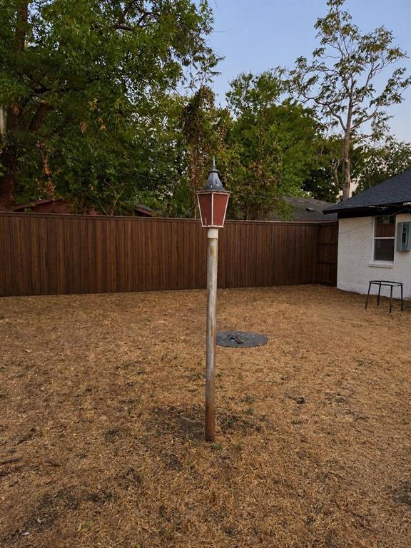 Backyard featuring a tall wood-finish privacy fence, a metal post-mounted lantern, and exterior white masonry