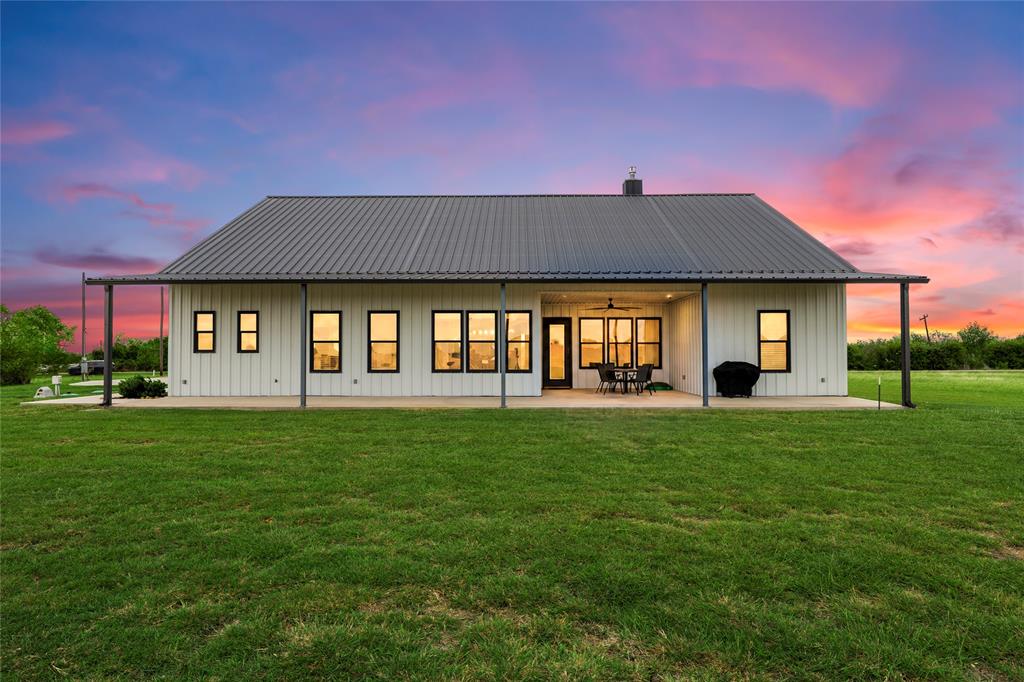 Modern exterior featuring vertical siding, a standing seam metal roof, a full-length covered patio, and large rectangular windows