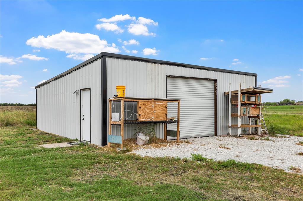 Detached metal-sided workshop featuring a roll-up bay door, a separate pedestrian entry door, and a gravel-surfaced approach