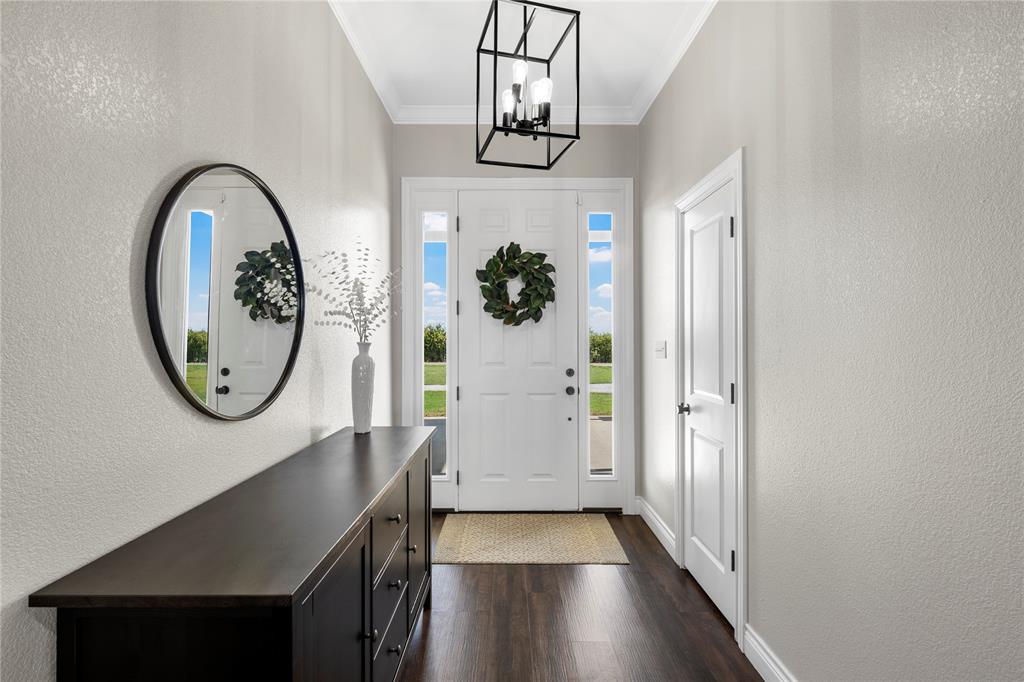 Foyer featuring wood-finish flooring, a white front door with flanking sidelights, crown molding, and a matte black geometric pendant light