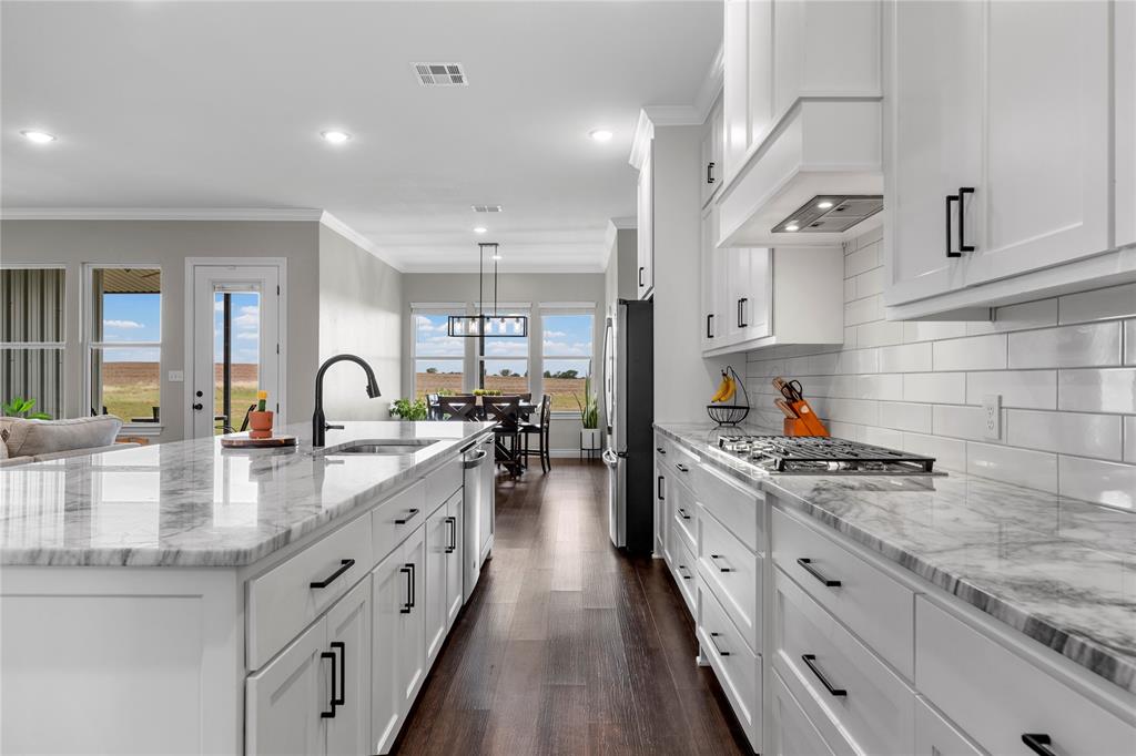 Kitchen featuring white cabinetry, stone countertops, a subway tile backsplash, a center island with a stainless steel sink, and wood-finish flooring