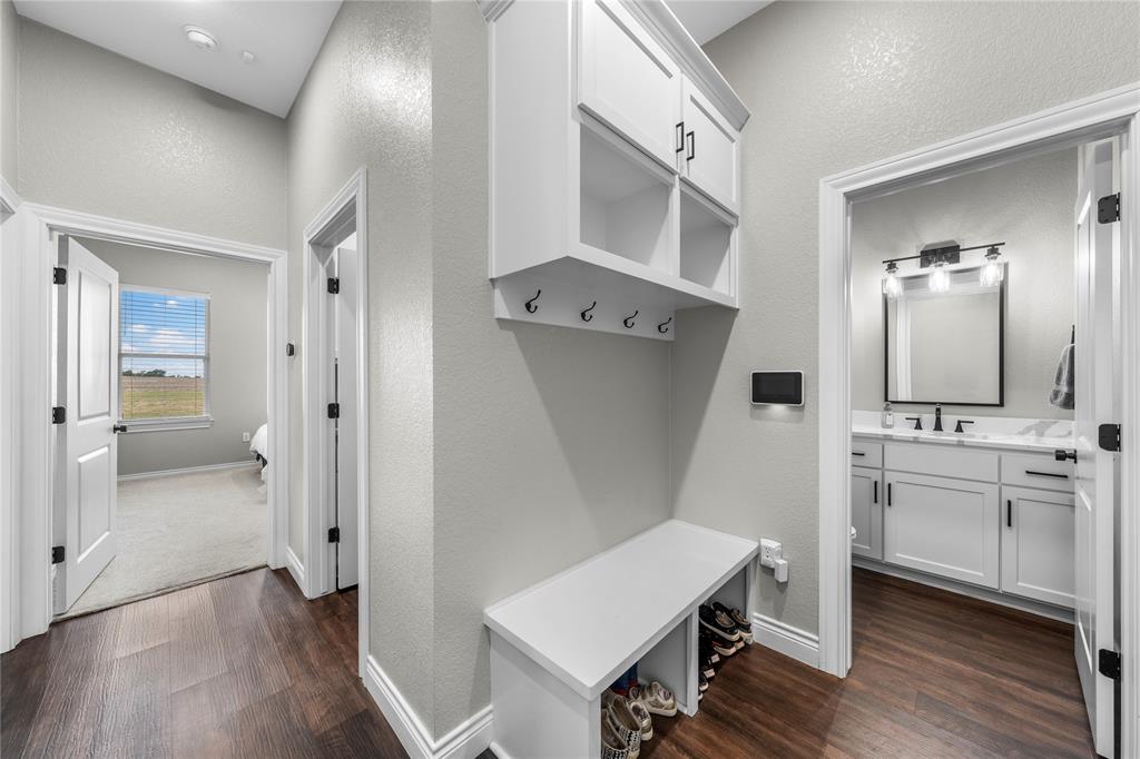 Built-in mudroom bench featuring upper cabinetry and wall-mounted hooks, wood-finish flooring, and shaker-style cabinetry