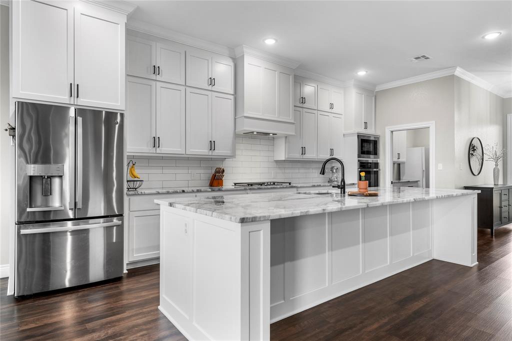 Kitchen featuring ceiling-height shaker cabinetry, stone-finish countertops, stainless steel appliances, a center island with sink, and wood-finish flooring
