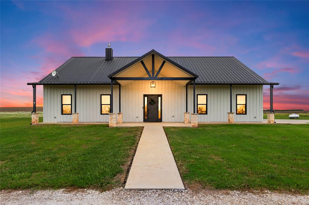 Single-story home featuring vertical siding, a metal roof, stone-based porch columns, and a covered entryway