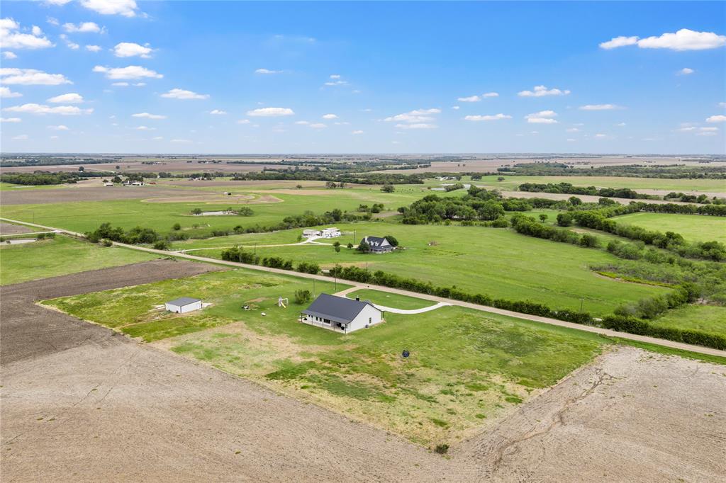 Aerial perspective featuring a multi-acre rural lot, a single-story residence with a metal roof, a secondary detached structure, and expansive open pasture land
