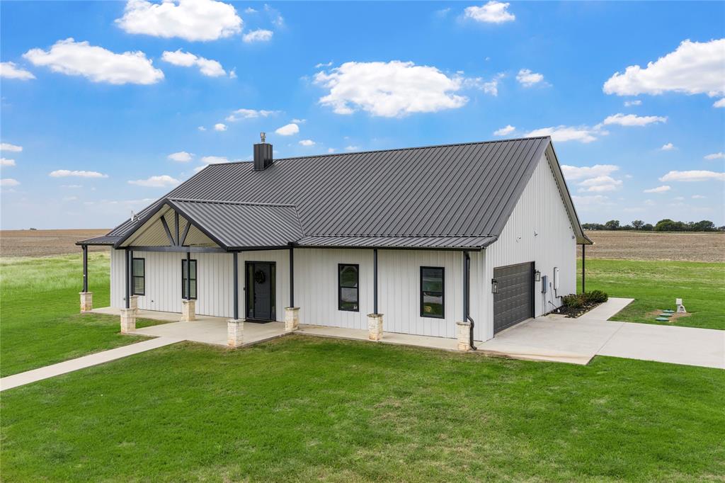Modern farmhouse exterior featuring vertical metal siding, a standing-seam metal roof, a covered front porch with stone-accented pillars, and an attached side-entry garage