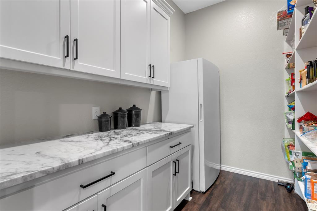 Walk-in pantry featuring white shaker-style cabinetry, stone-patterned countertops, dark hardware, wood-finish flooring, and open shelving
