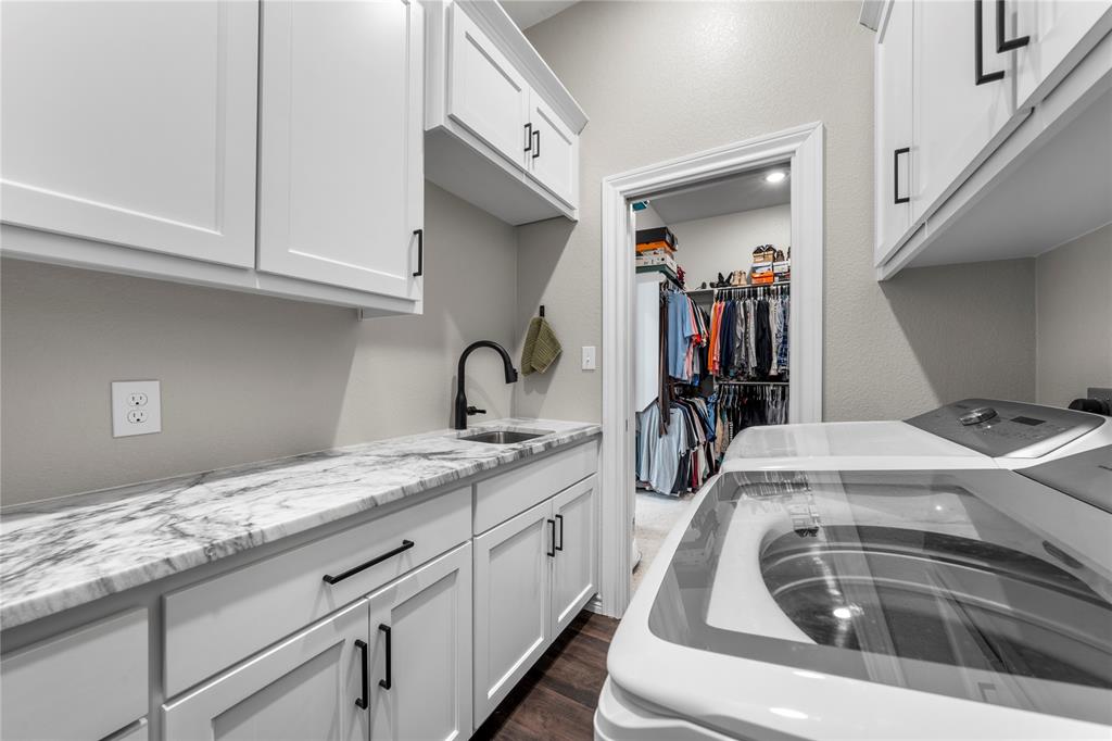 Laundry room featuring white shaker-style cabinetry, stone-finish countertops, an undermount sink with a matte black faucet, and wood-finish flooring