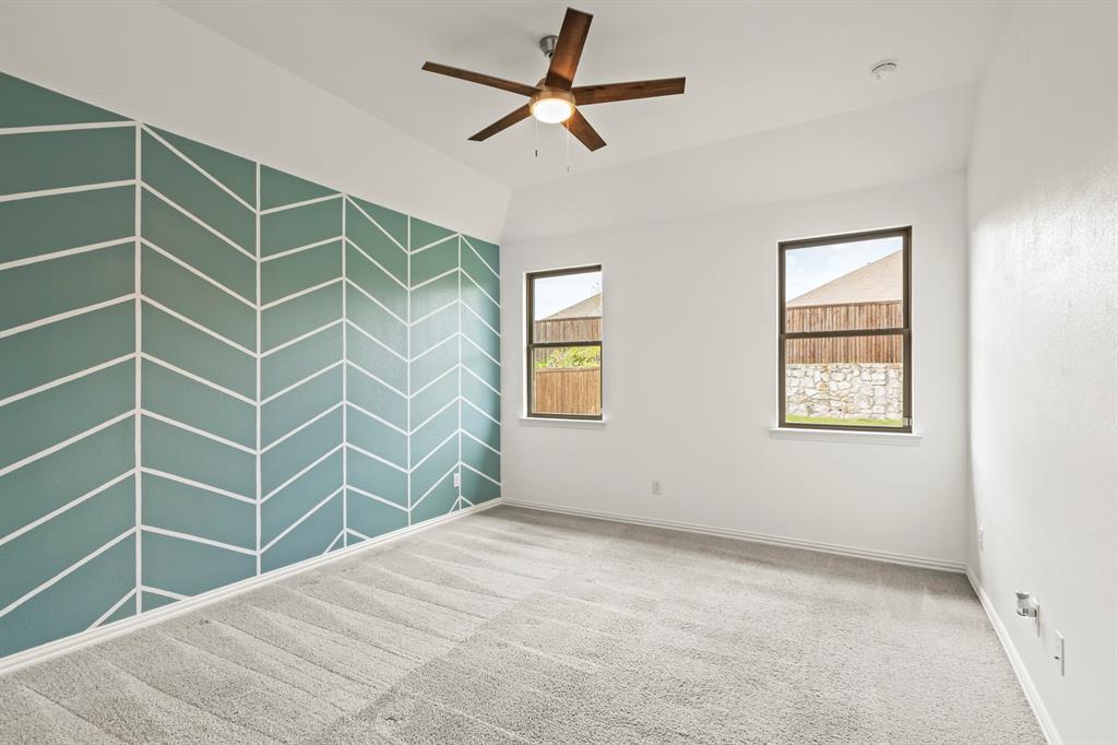 Room featuring tray ceilings, neutral carpeting, a dual-tone geometric accent wall, and a central ceiling fan with integrated lighting