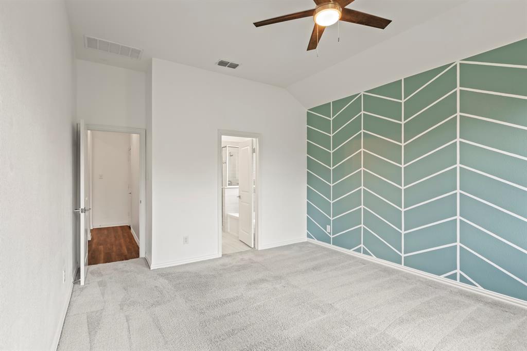 Vaulted ceilings featuring an integrated ceiling fan with light fixture, decorative accent wall with geometric pattern, and neutral carpeting
