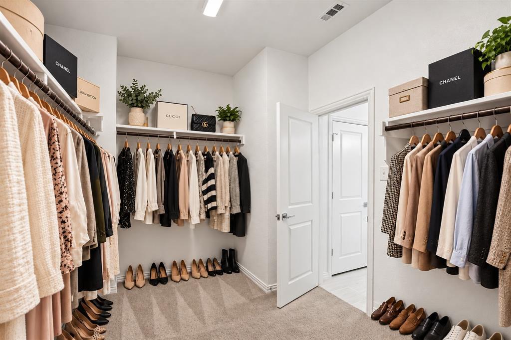 Walk-in closet featuring multi-level built-in shelving, hanging rods, neutral carpeting, and a multi-panel door. Virtual photo